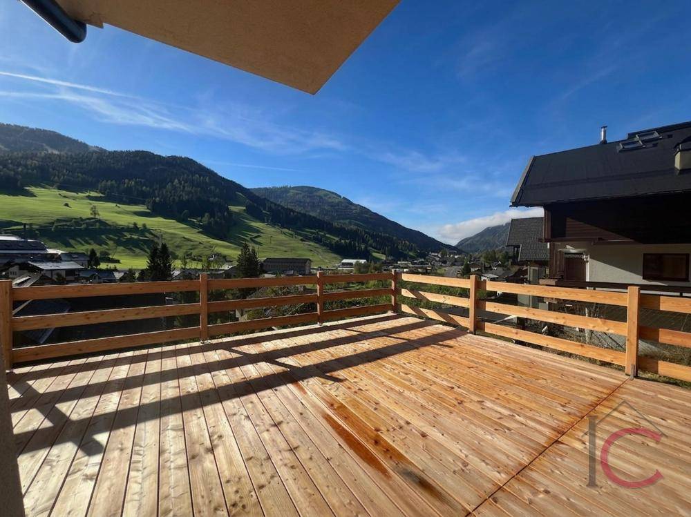 Geräumige Holzterrasse mit Panoramablick auf die Berge unter blauem Himmel und Sonnenschein.