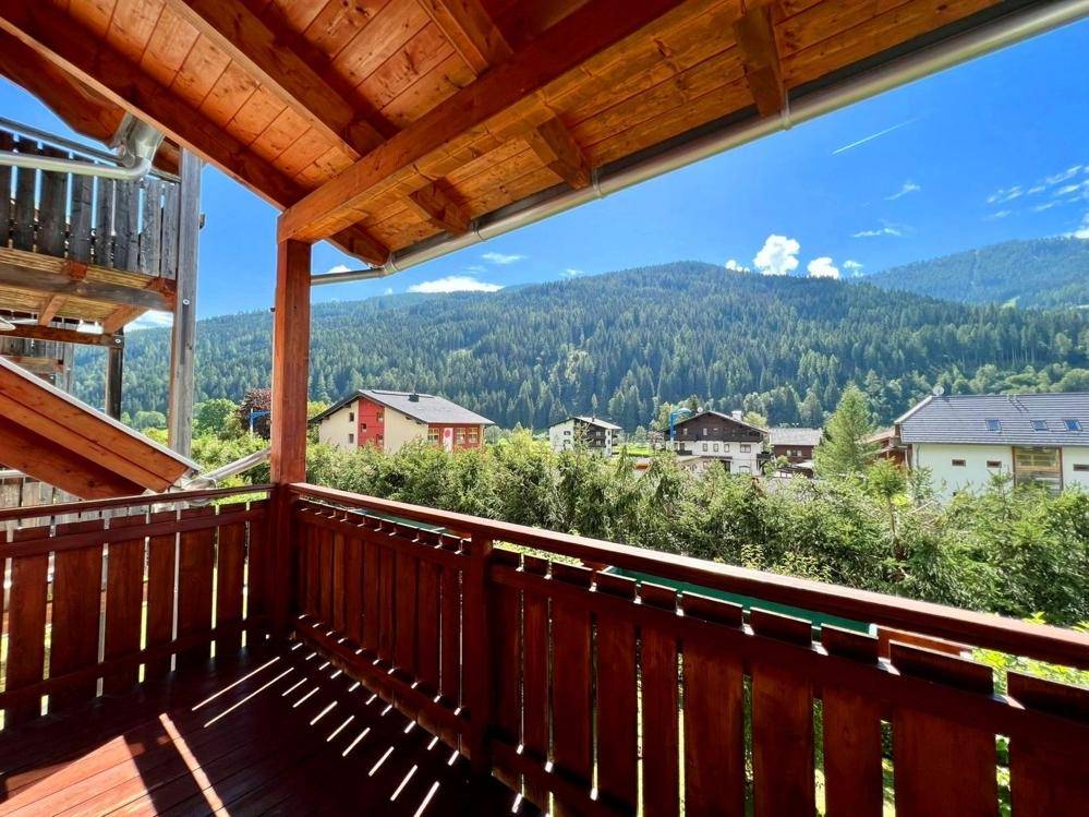 Sonniger Holzbalkon mit weitem Blick auf die umliegenden Berge und grüne Landschaft.