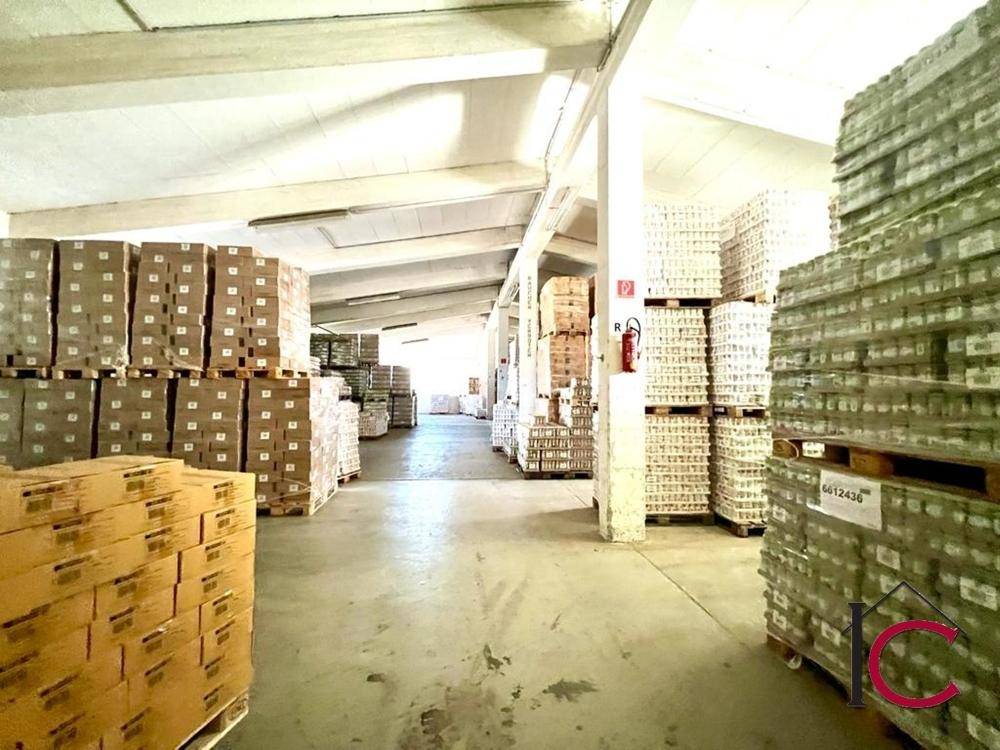 Weitläufige Lagerhalle mit schrägen Dächern, Betonboden und hohen Stapeln von Waren.
