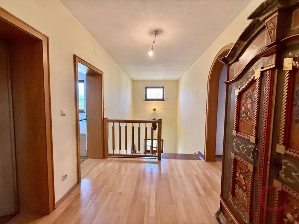 Obergeschoss-Flur mit Holzparkettboden, Holzgeländer und einem dekorativen Schrank.