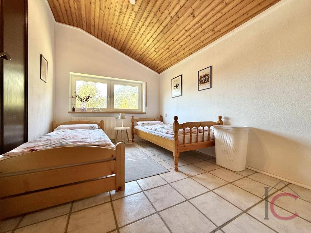 Helles Schlafzimmer mit zwei Einzelbetten, Holzdecke und Fenster mit Blick ins Grüne.