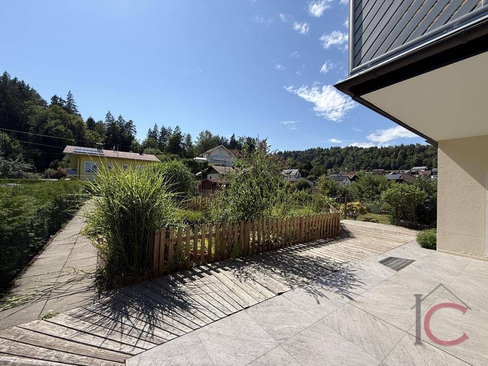 Großzügige Terrasse mit kombiniertem Fliesen- und Holzdeck, umgeben von üppiger Natur und Sonne.