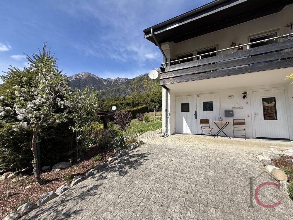 Seitenansicht des Hauses mit gepflasterter Fläche, kleinem Sitzbereich und Bergblick.