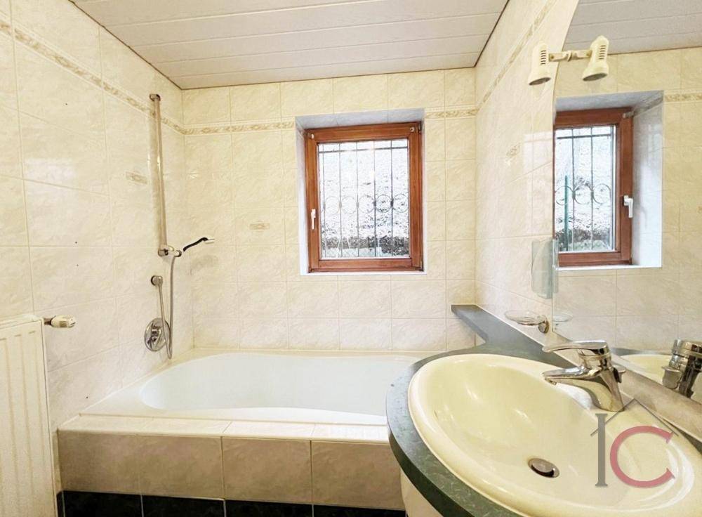 Helles Badezimmer mit Badewanne, Waschbecken und Fenster, komplett gefliest.