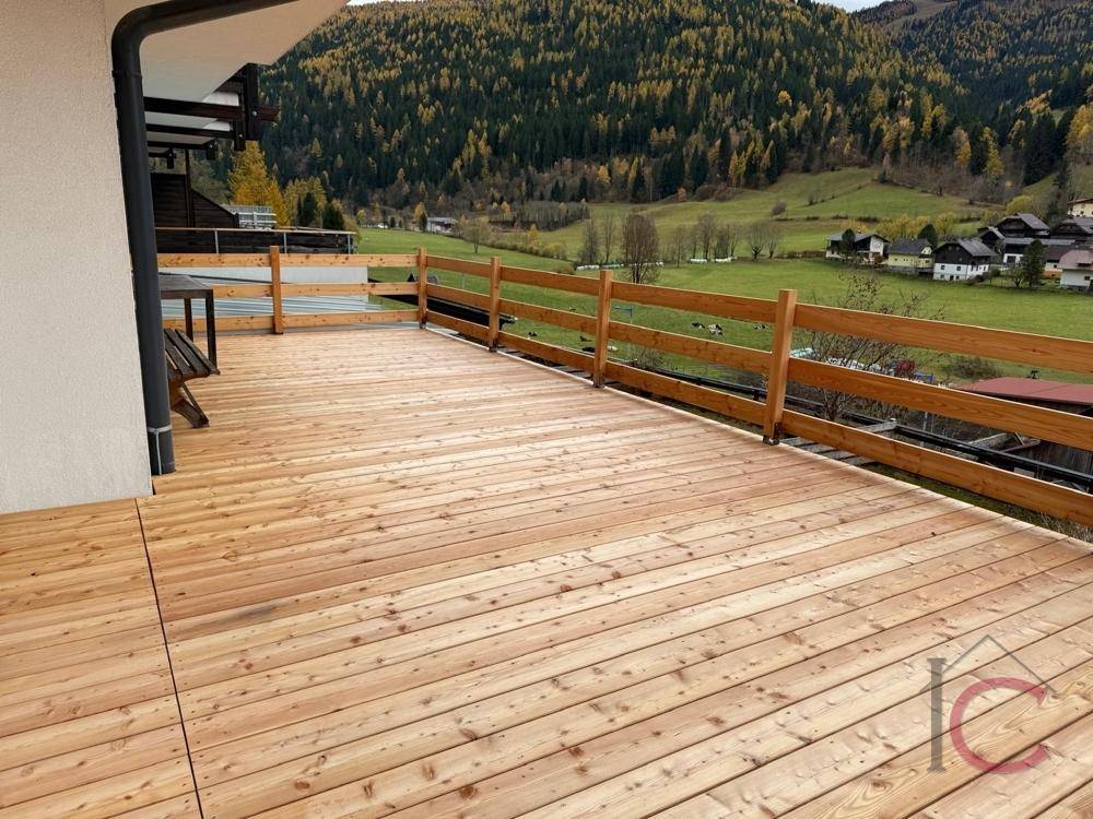 Geräumige Holzterrasse mit Panoramablick auf grüne Hügel und die umliegende Landschaft.