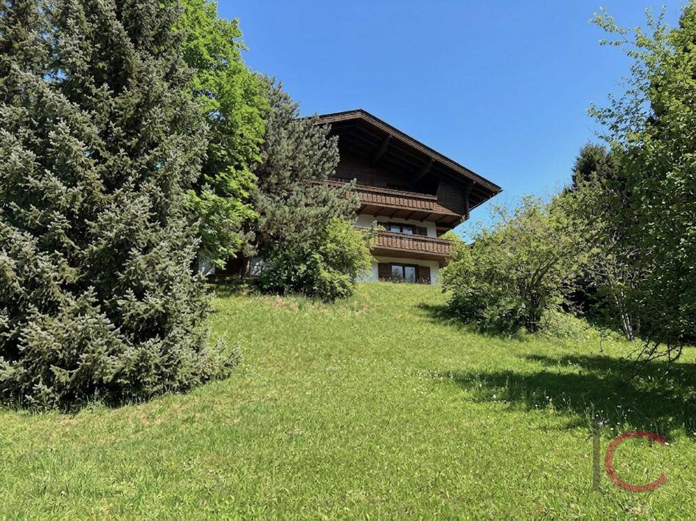 Traditionelles Haus auf einem grünen Hügel, umgeben von Bäumen und Natur.