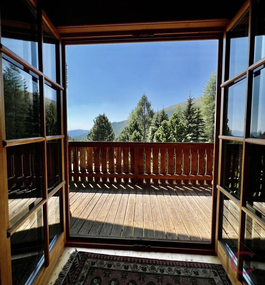 Sonniger Holzbalkon mit weitem Blick auf die umliegende Berglandschaft und dichte Wälder.
