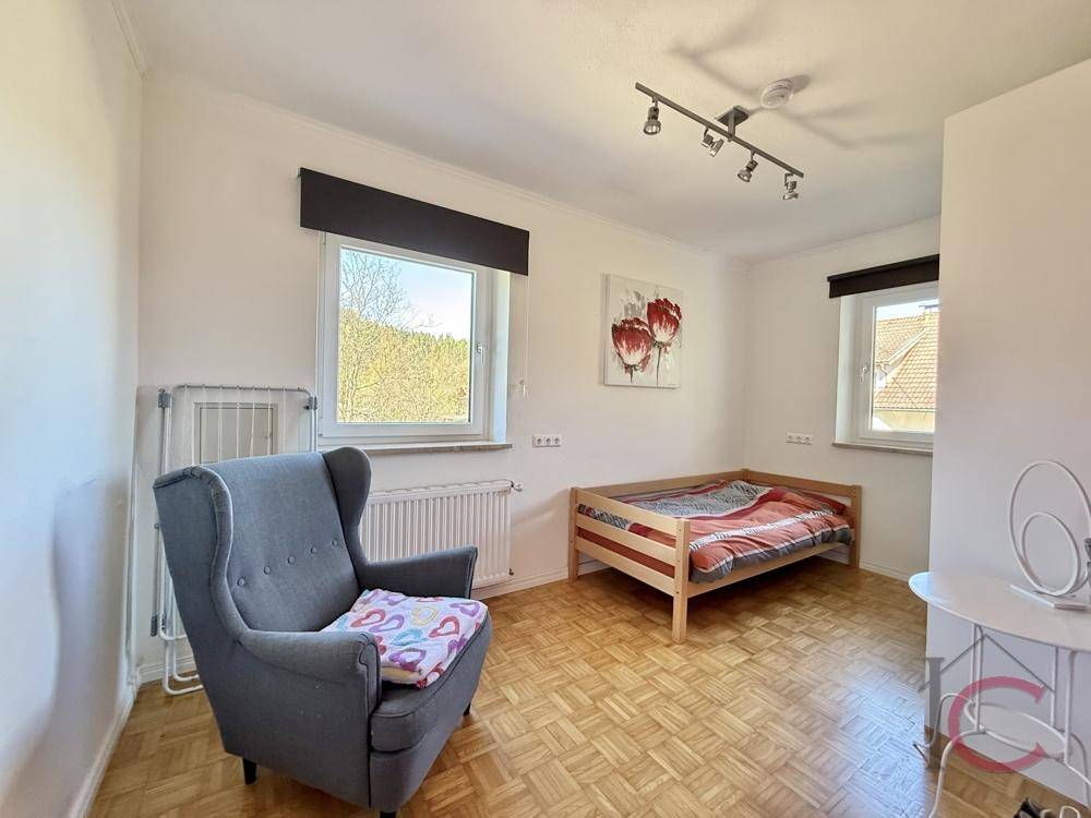 Helles Schlafzimmer mit Einzelbett, bequemem Sessel und Parkettboden, ideal als Gästezimmer.