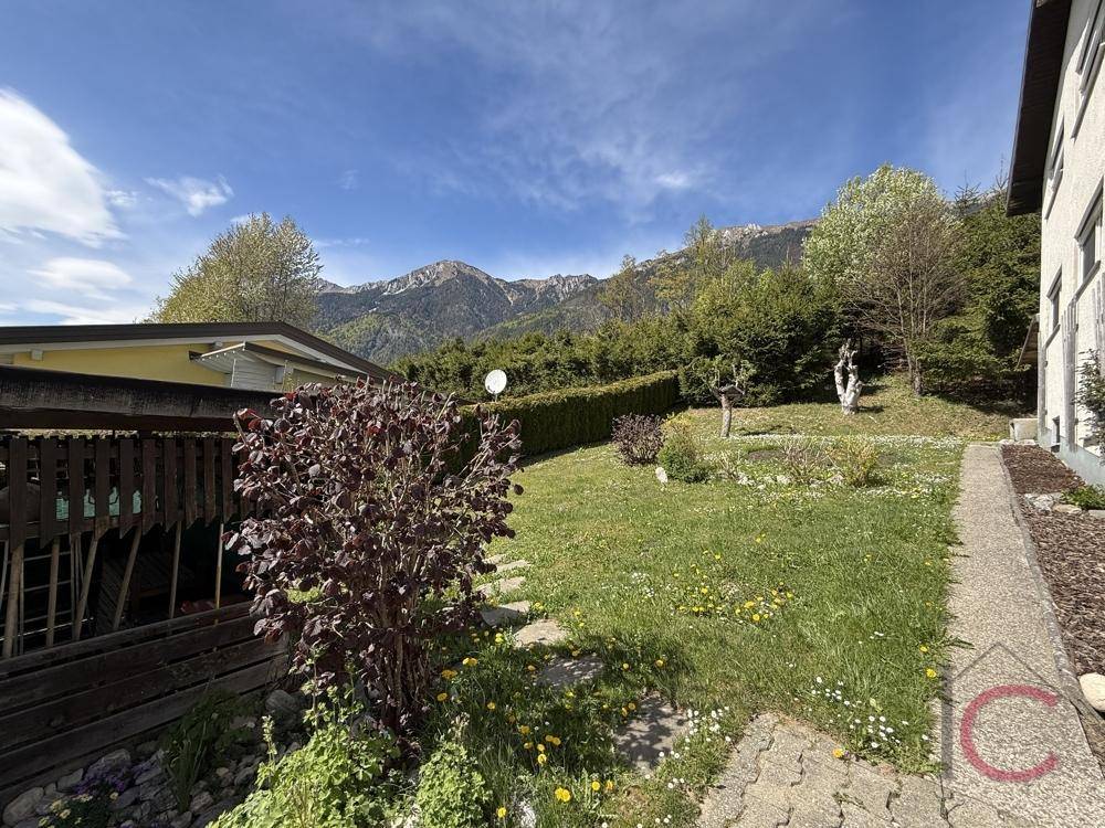 Gepflegter Gartenbereich mit Rasen, Hecke und Blick auf die umliegenden Berge.