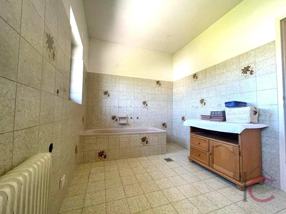 Geräumiges Badezimmer mit Badewanne und floral gemusterten Fliesen, ausgestattet mit einem Fenster.