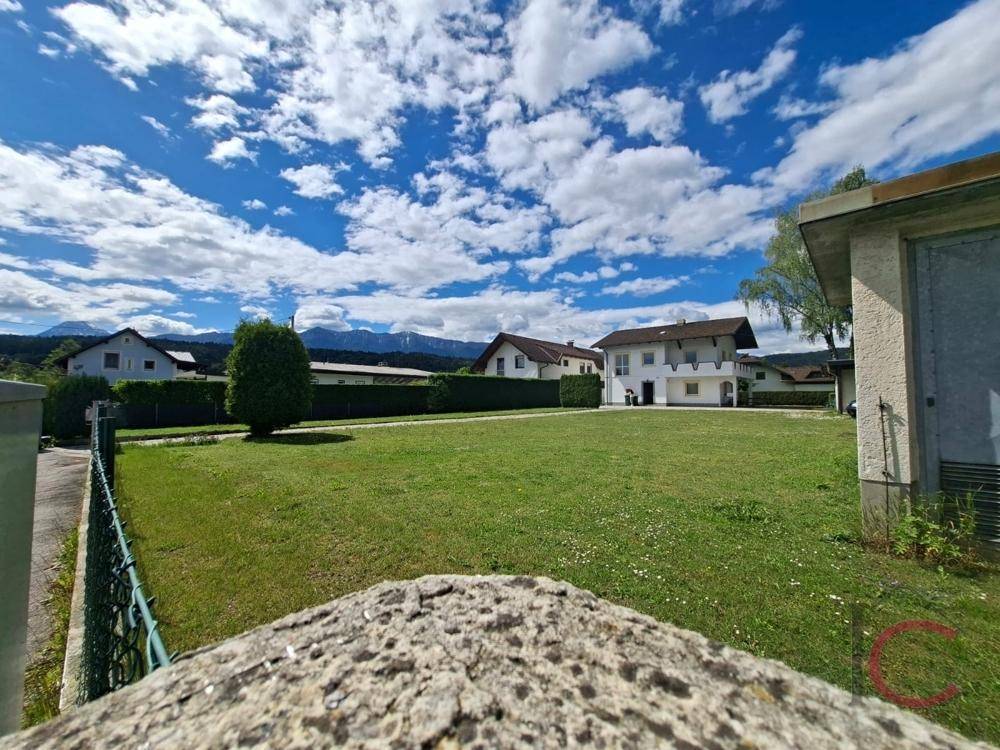 Weitläufige Grünfläche mit Blick auf die umliegende Nachbarschaft und ferne Berge unter blauem Himmel.