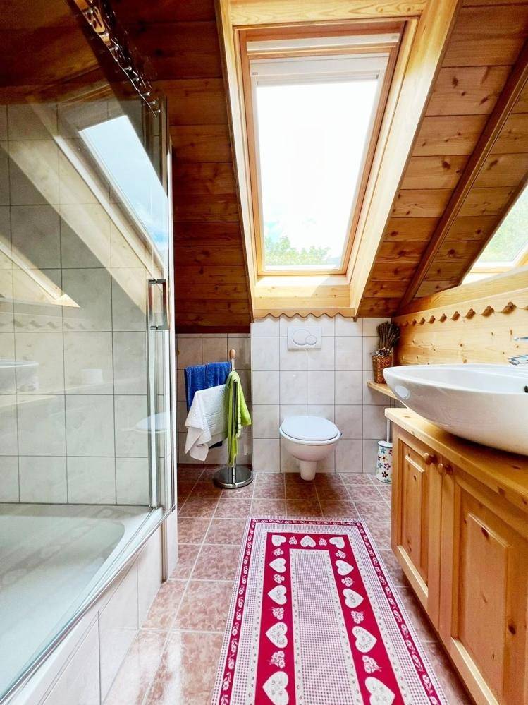 Badezimmer mit Dachfenster, Duschkabine und traditionellen Fliesen und Holzmöbeln.
