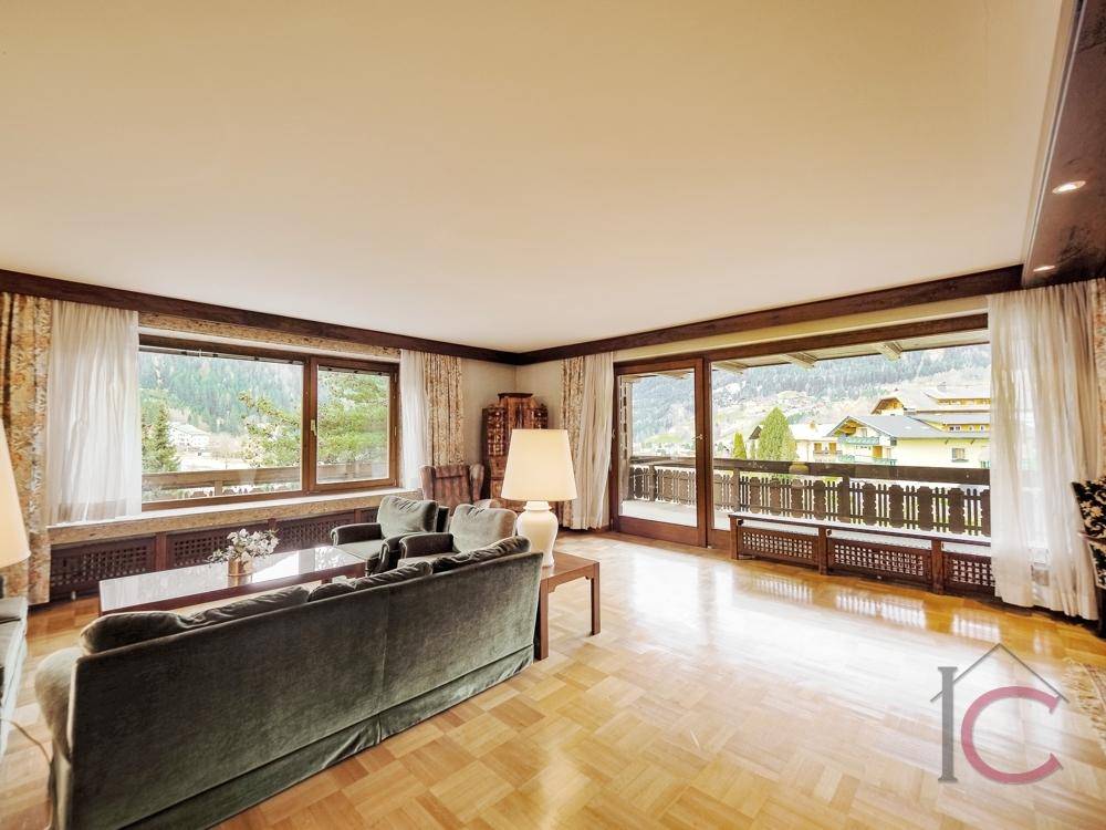 Lichtdurchflutetes Wohnzimmer mit Parkettboden und Zugang zu einem Balkon mit Bergblick.