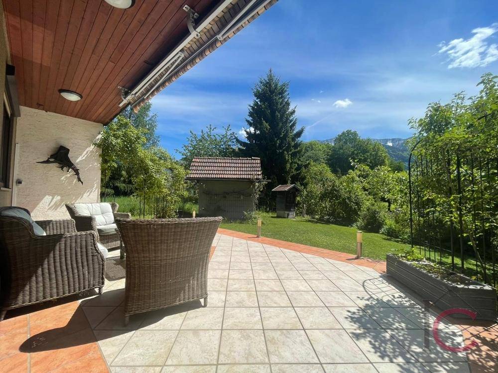 Sonniger Terrassenbereich mit Korbmöbeln und weitem Blick über den Garten und die Berge.