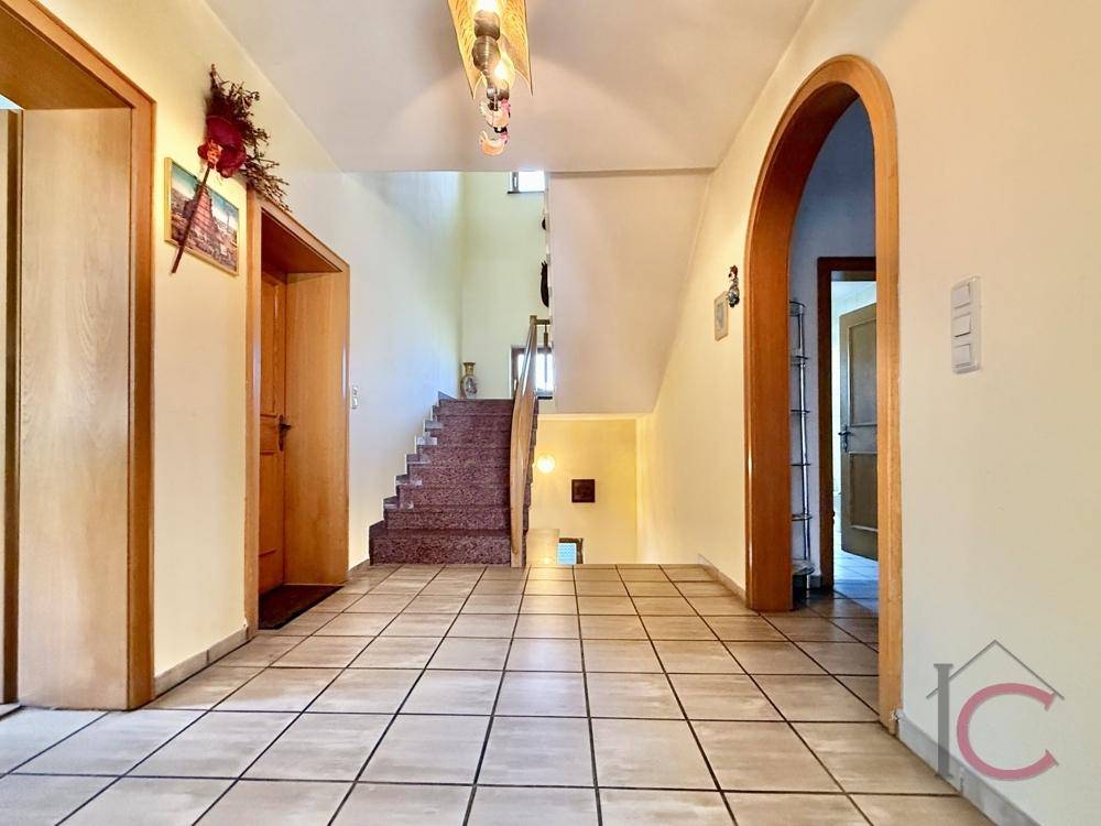Geräumiger Eingangsbereich mit Fliesenboden, Holztüren und einer Treppe zum Obergeschoss.