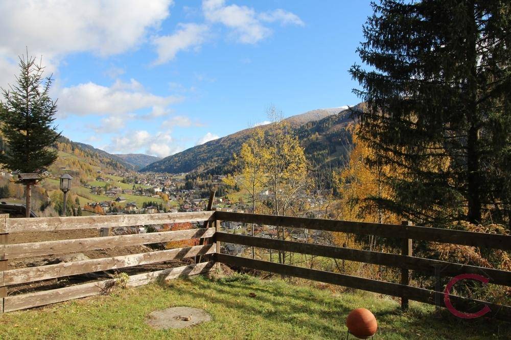 Malerischer Ausblick auf ein Dorf im Tal, umgeben von grünen Hügeln und Bergen.