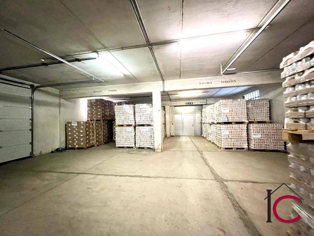 Großer Lagerraum mit hohen Decken, Betonboden und zahlreichen gestapelten Kartons und Paletten.