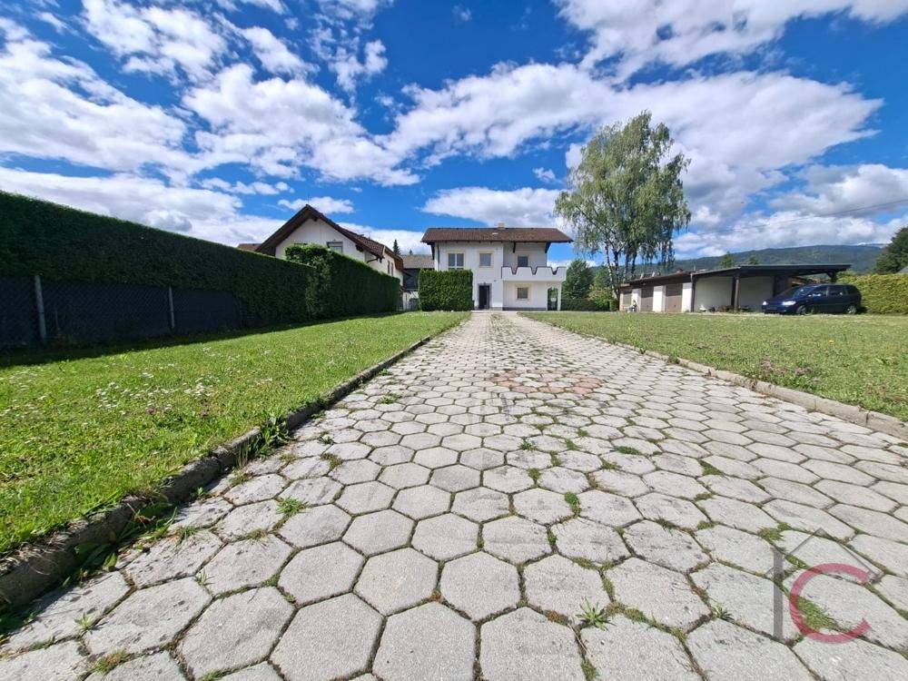 Zufahrt zum Haus mit sechseckigen Pflastersteinen, umgeben von Rasenflächen und Hecken.