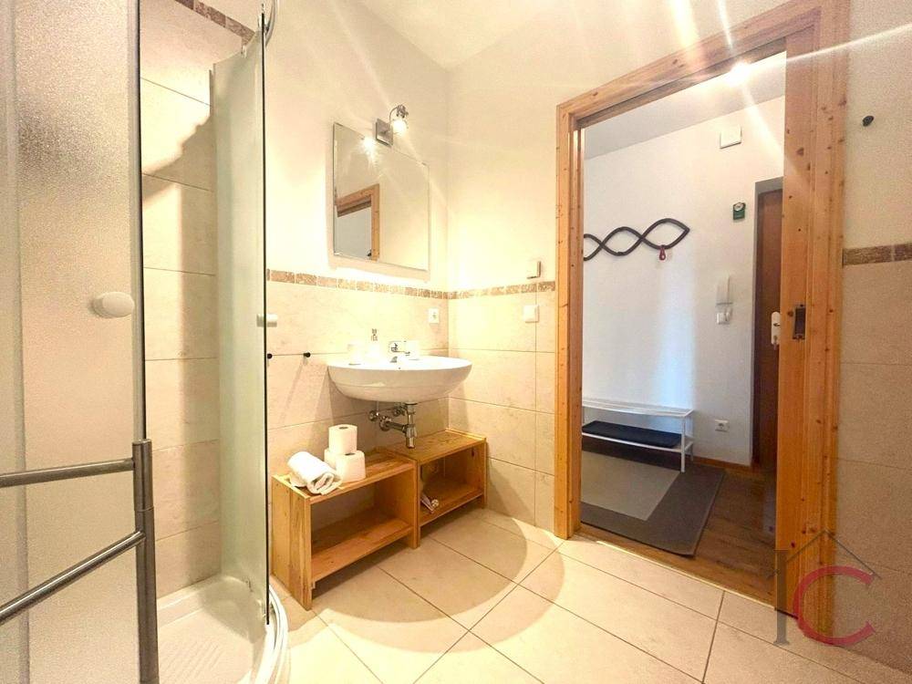 Modernes Badezimmer mit Duschkabine, Waschbecken und hellen Fliesen an Wänden und Boden.