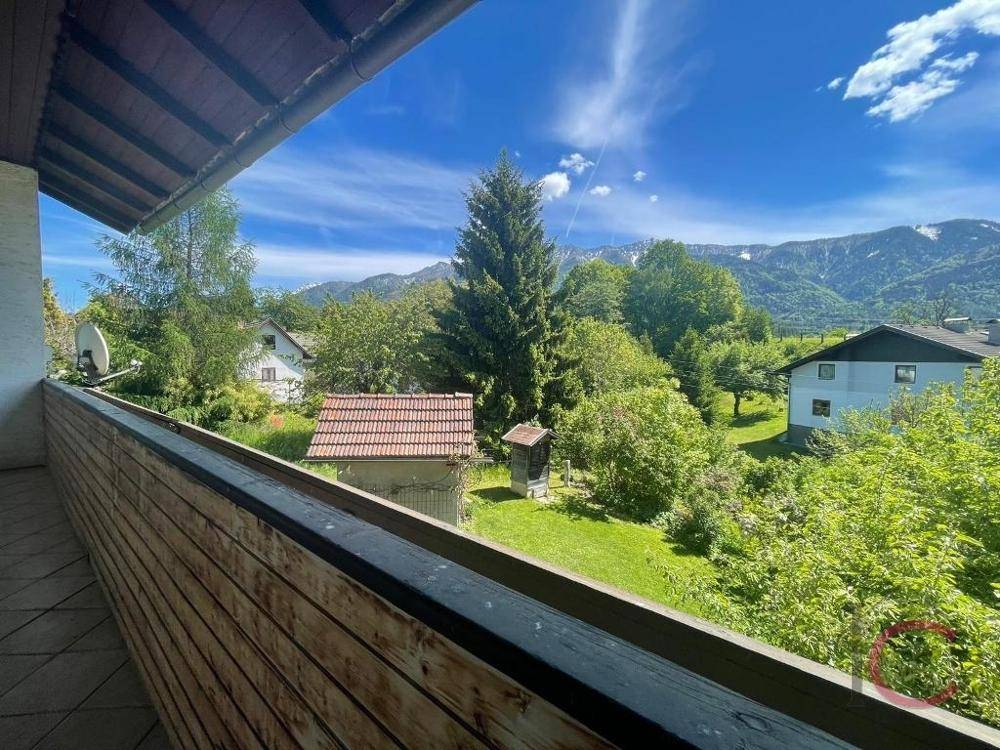 Balkon mit Holzgeländer und weitem Blick über den Garten und die umliegenden Berge.