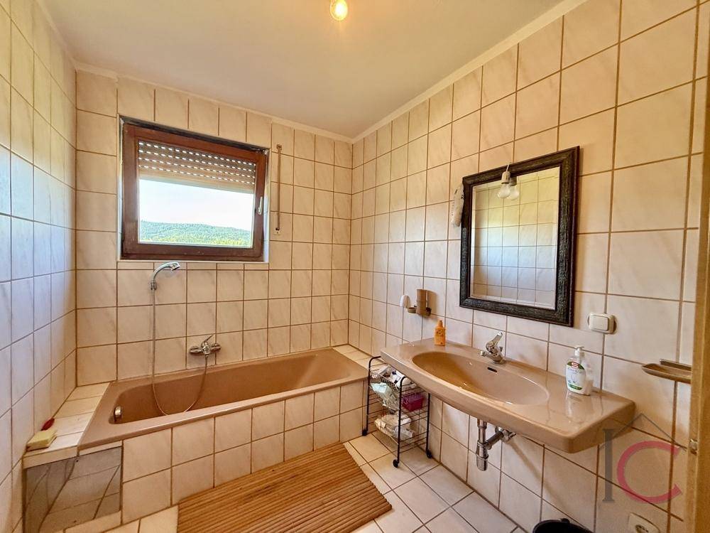 Badezimmer mit beigefarbenen Fliesen, Badewanne, Einzelwaschbecken und Fenster.