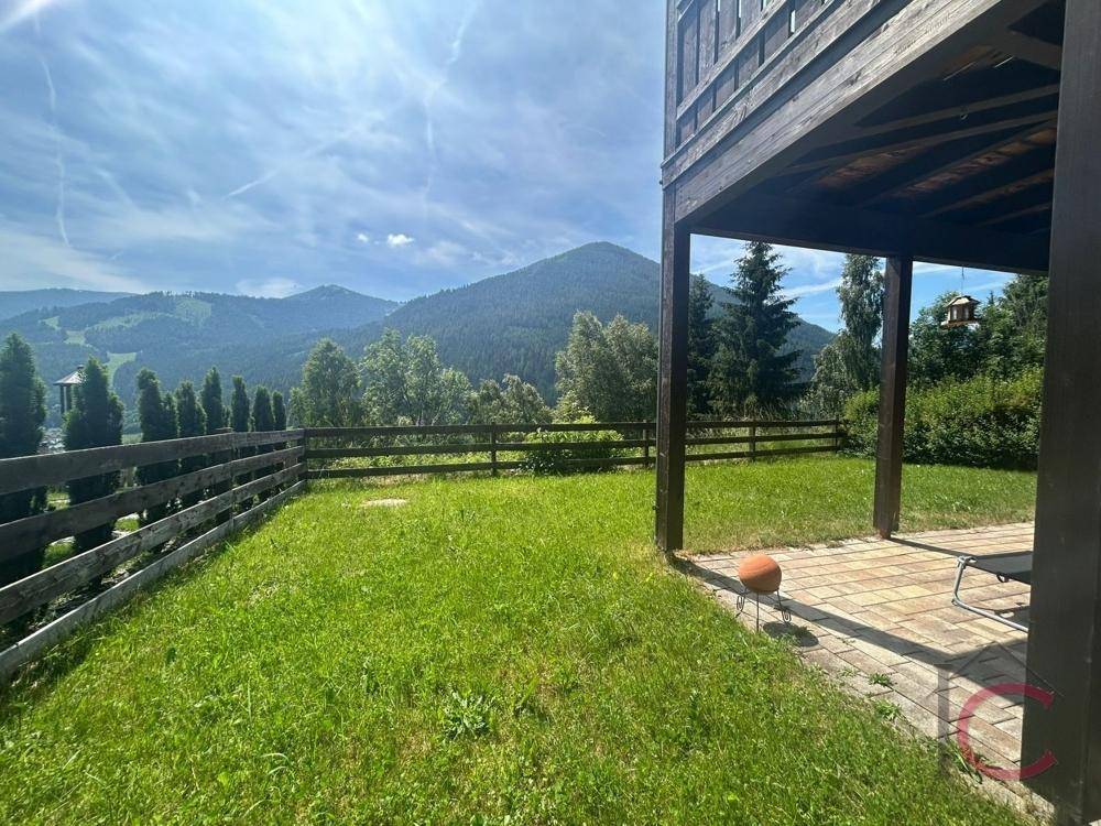 Gepflegter Rasenbereich mit teilweiser Überdachung und weitem Blick auf die grüne Berglandschaft.