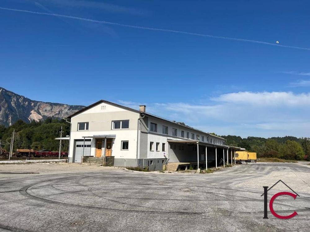 Ansicht des Industriegebäudes mit Laderampen und großem Vorplatz vor bergiger Landschaft.