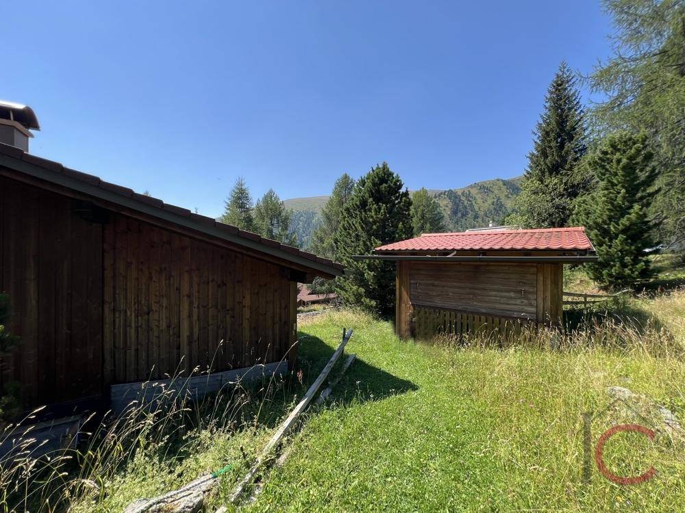 Zwei rustikale Holzschuppen in einer grünen Wiesenlandschaft unter klarem Himmel.