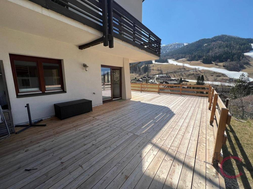 Große Holzterrasse mit weitem Blick auf die schneebedeckten Berge und Skipisten.