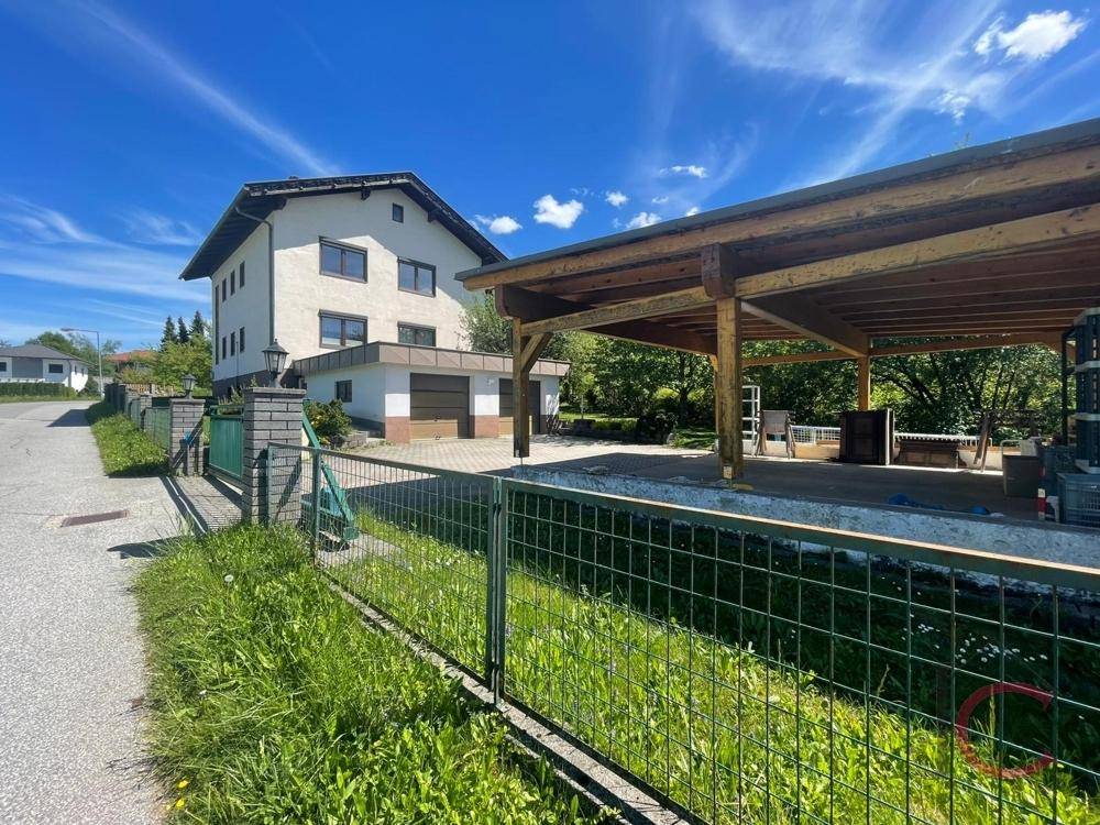 Wohnhaus mit Doppelgarage und Holzcarport, umgeben von einem Zaun und grüner Landschaft.