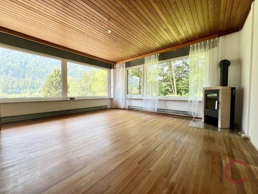 Geräumiger Raum mit Holzboden, großen Fenstern und einem modernen Kaminofen.