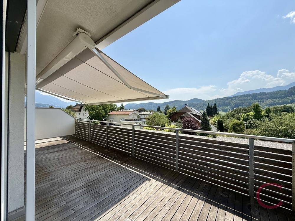 Sonnige Terrasse mit Holzboden und Markise, bietet einen schönen Ausblick auf die umliegende Landschaft.