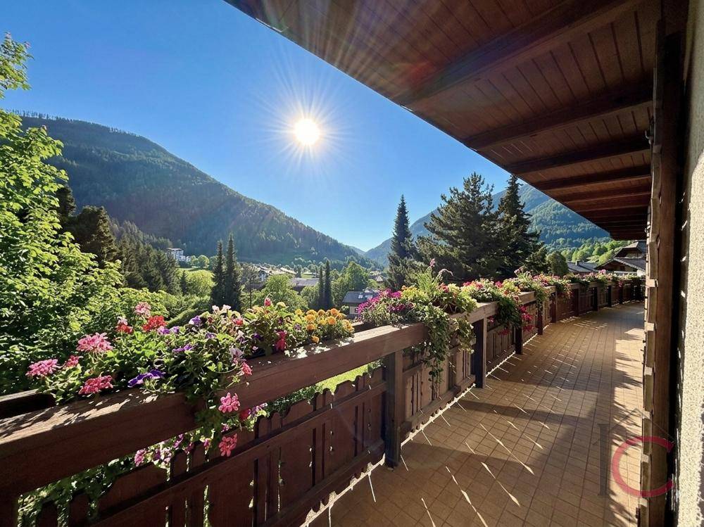 Langer Balkon mit Blumenkästen und sonnigem Ausblick auf die umliegende Berglandschaft.