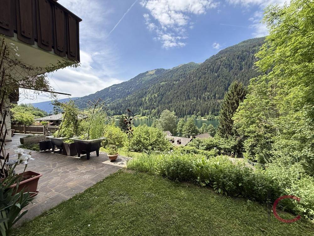 Gepflegter Gartenbereich mit Rasenfläche und Blick auf den See und die bewaldeten Berge.