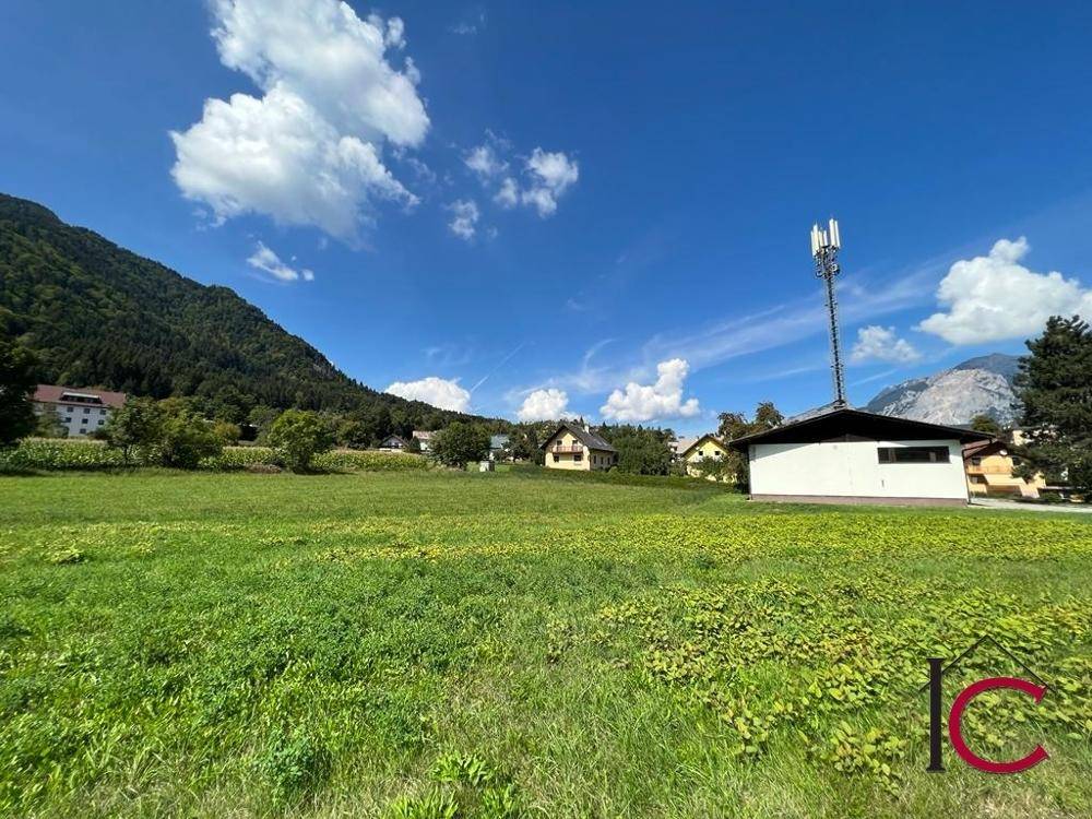 Grüne Wiesenlandschaft mit Bergen im Hintergrund und einem Mobilfunkmast unter blauem Himmel.