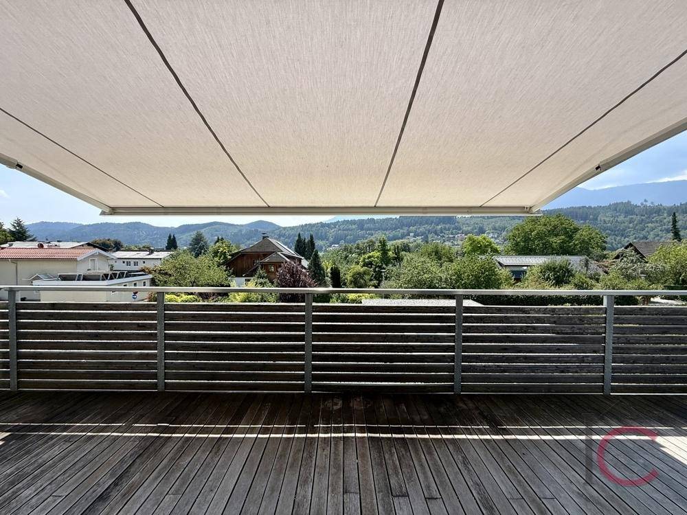 Geräumige Holzterrasse mit ausfahrbarer Markise und weitem Blick ins Grüne und auf die Berge.