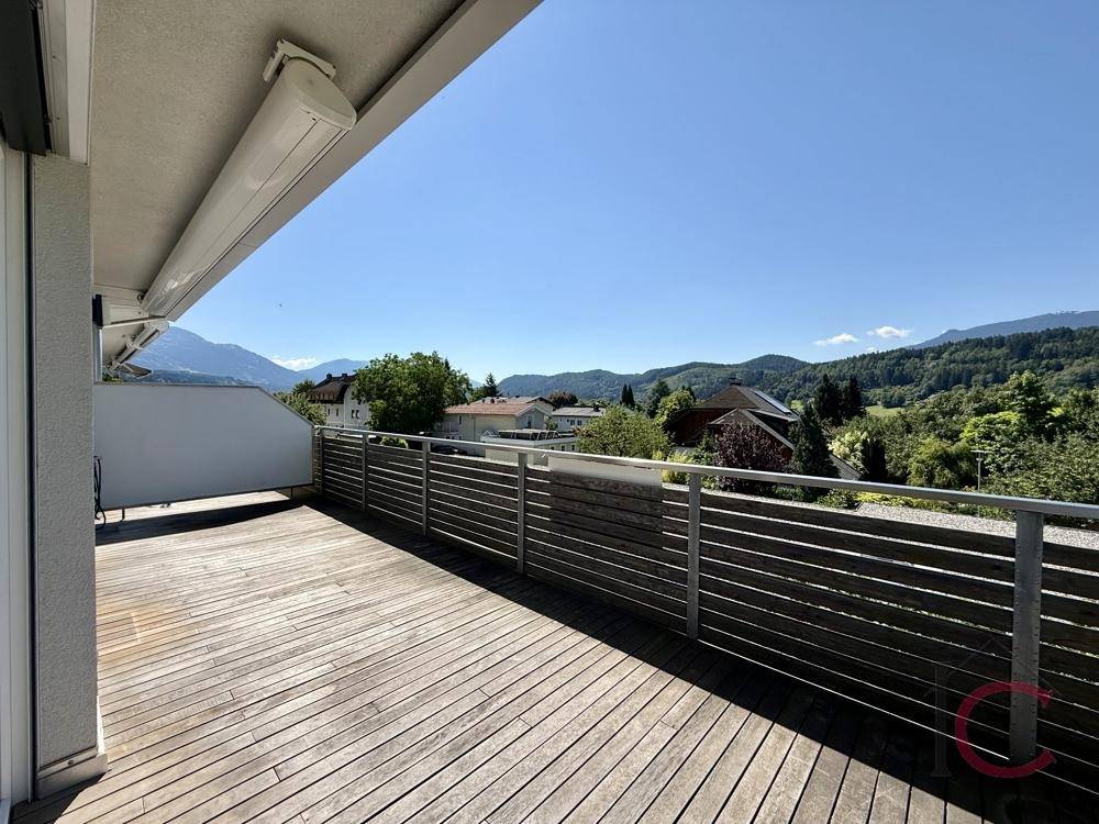 Sonnige Holzterrasse mit weitem Blick über die Landschaft und die fernen Berge.