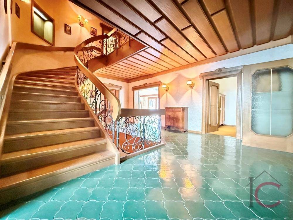 Elegante Eingangshalle mit geschwungener Holztreppe, schmiedeeisernem Geländer und gemusterten Fliesen.