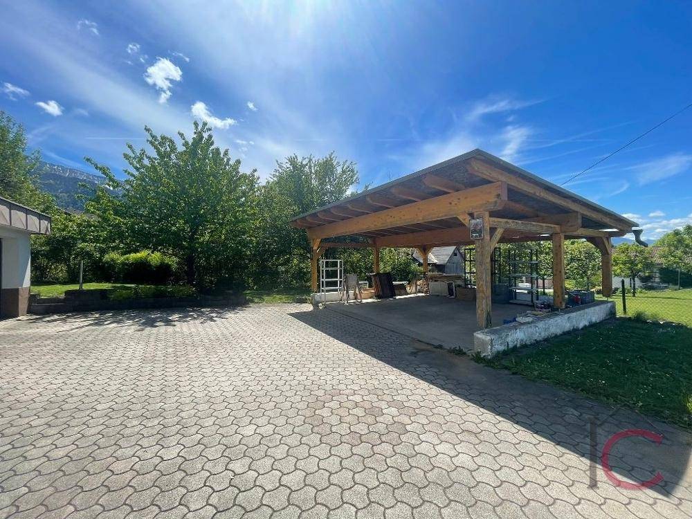 Großer Holzcarport mit gepflasterter Einfahrt und grüner Umgebung unter blauem Himmel.