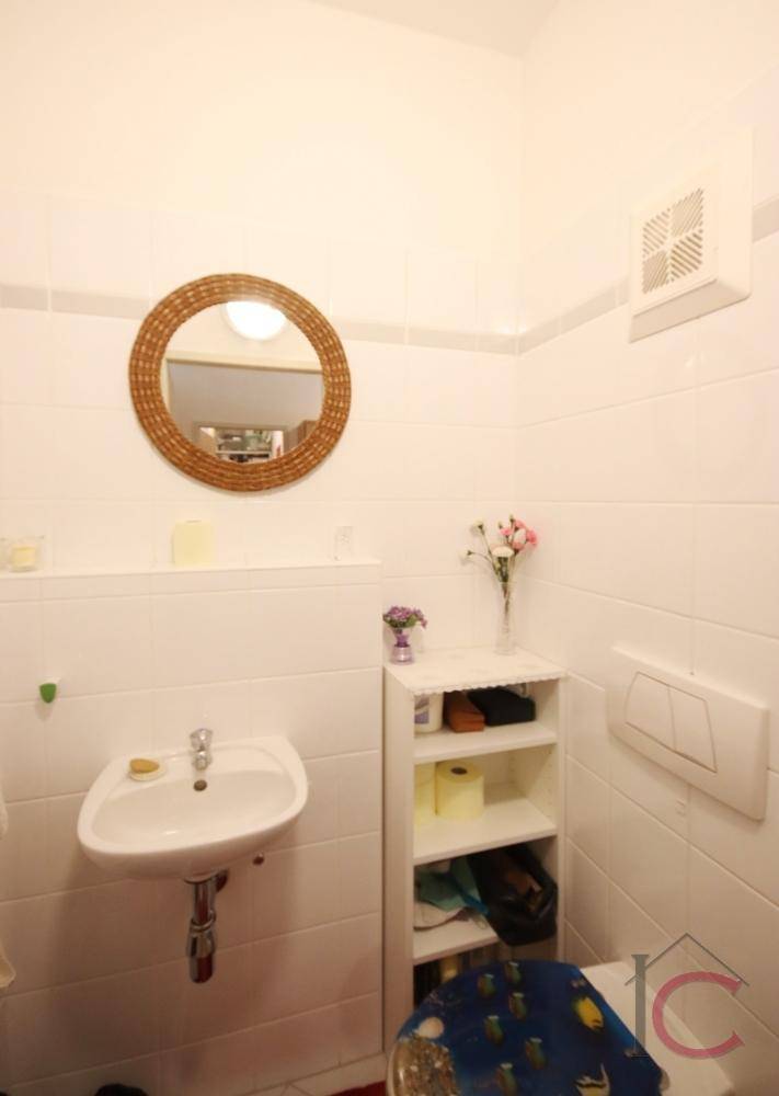 Helles WC mit Waschbecken, wandhängender Toilette und rundem Spiegel, ausgestattet mit Ablageregal.