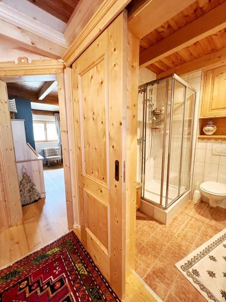 Heller Flur mit Holztür und Blick in ein Badezimmer mit Duschkabine.