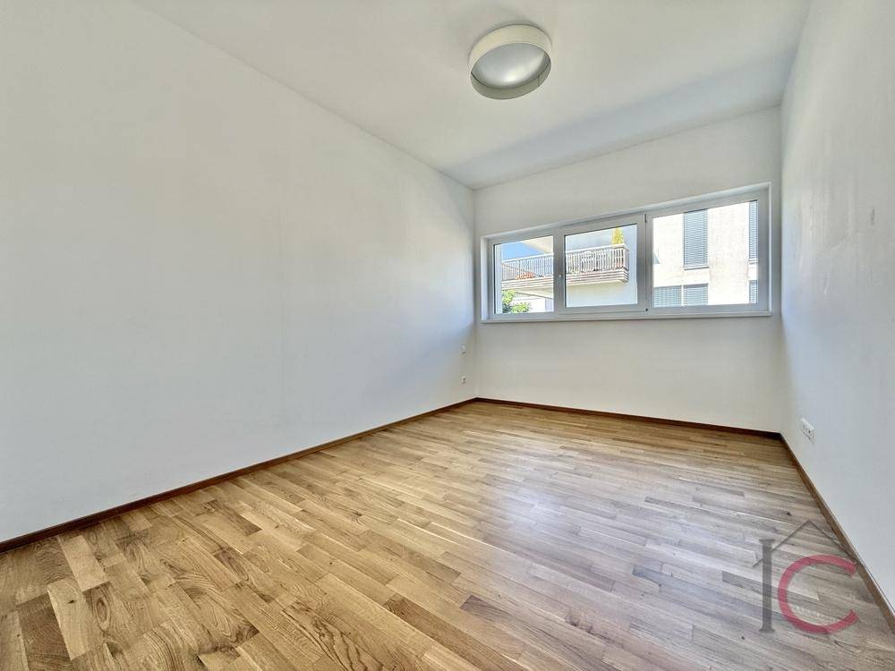 Leeres Zimmer mit Holzboden und großen Fenstern, ideal als Schlaf- oder Arbeitszimmer.