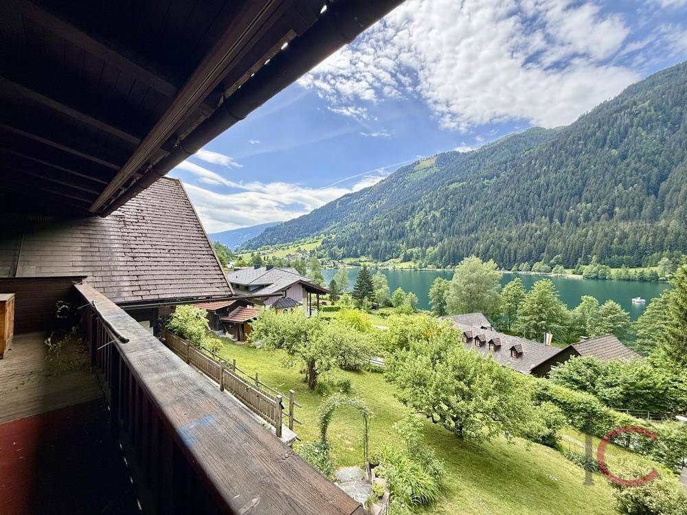 Balkon mit Holzgeländer und weitem Blick auf den See und die umliegende Berglandschaft.
