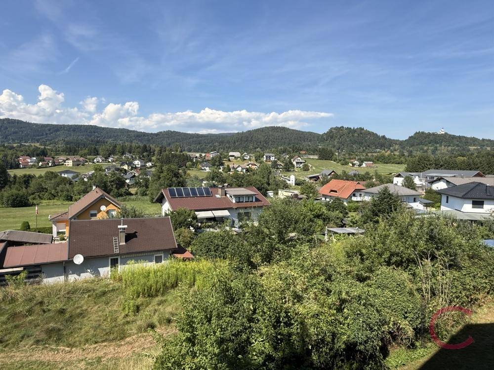 Weitläufiger Blick über eine ländliche Siedlung mit grünen Hügeln im Hintergrund.