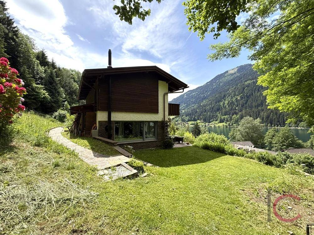Seitlicher Blick auf das Haus mit Garten, umgeben von Natur und mit Seeblick.