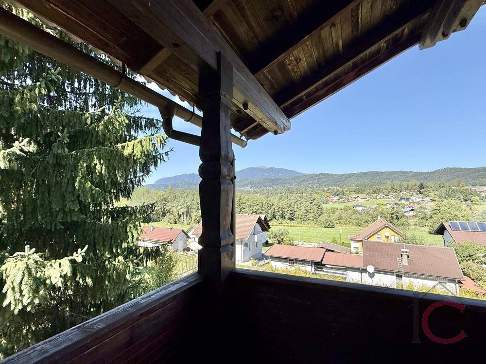Blick vom Holzbalkon auf die umliegende grüne Landschaft und die Dächer der Nachbarhäuser.