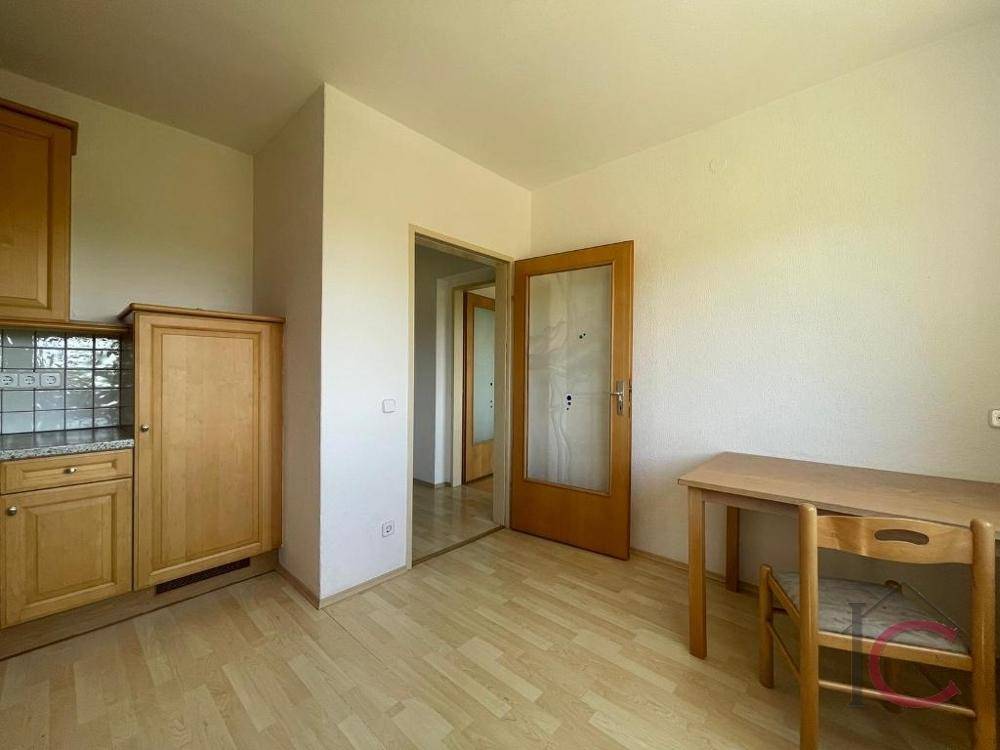 Küchenbereich mit Holzeinbauten und Essplatz, angrenzend an einen weiteren Raum.
