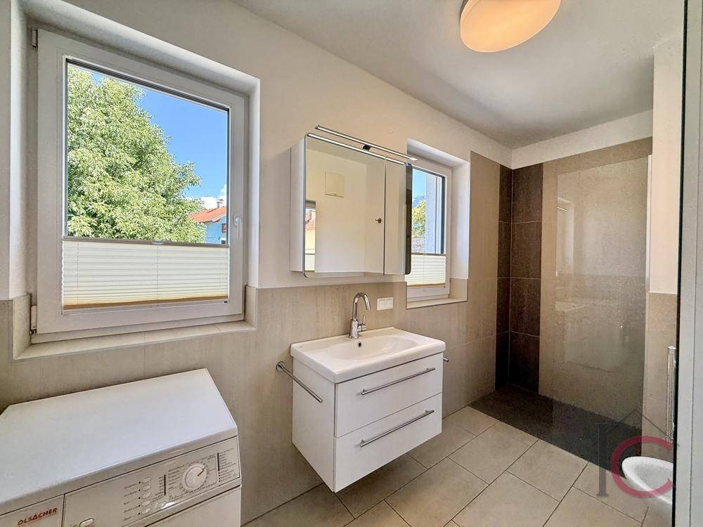Modernes Badezimmer mit Dusche, Waschbecken, Spiegelschrank und Fenster.