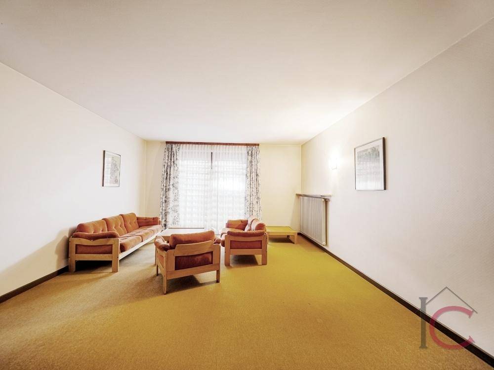 Helles Wohnzimmer mit gelbem Teppichboden und einfacher, funktionaler Einrichtung.