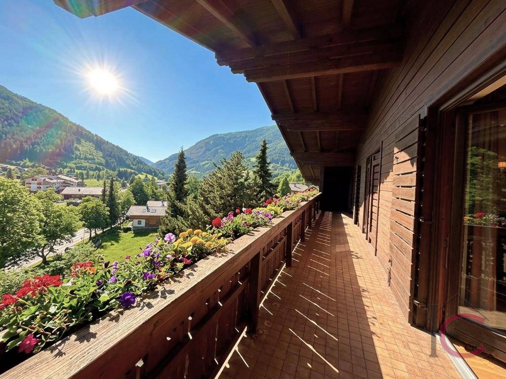 Sonniger Balkon mit Holzverkleidung, Blumenkästen und weitem Blick ins Tal.